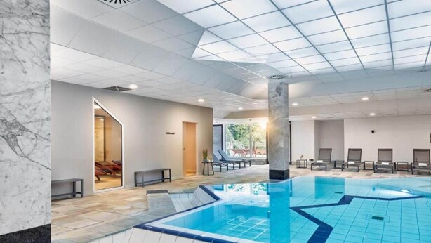 A swimming pool with a tiled floor, a ceiling with a grid pattern, and a door leading to an outdoor area.