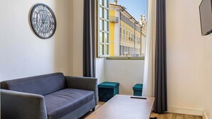 Ett modernt vardagsrum med en soffa, ett soffbord, en klocka och utsikt över en byggnad genom ett fönster.