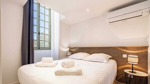 Ett hotellrum med en stor säng, en sänglampa, en luftkonditioneringsanläggning och ett fönster med gardiner.