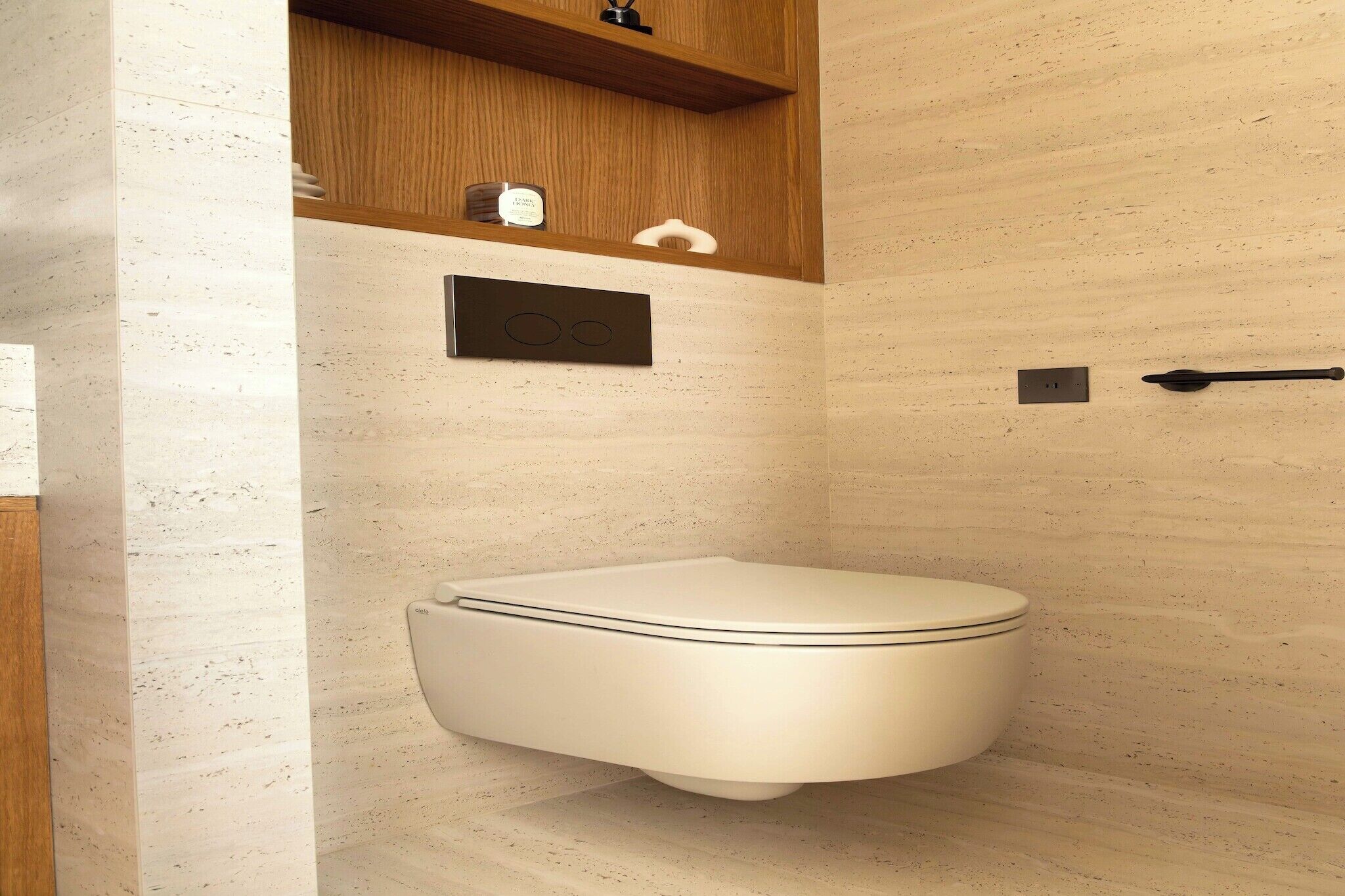 Une salle de bain moderne avec des toilettes, une étagère sur laquelle est posée une bougie et un porte-serviettes fixé au mur.