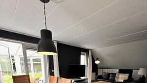 A modern living room with a dining area, large windows, and a flat-screen TV. - Vacation villa with conservatory at the 't Posterbos park (Posterholt)