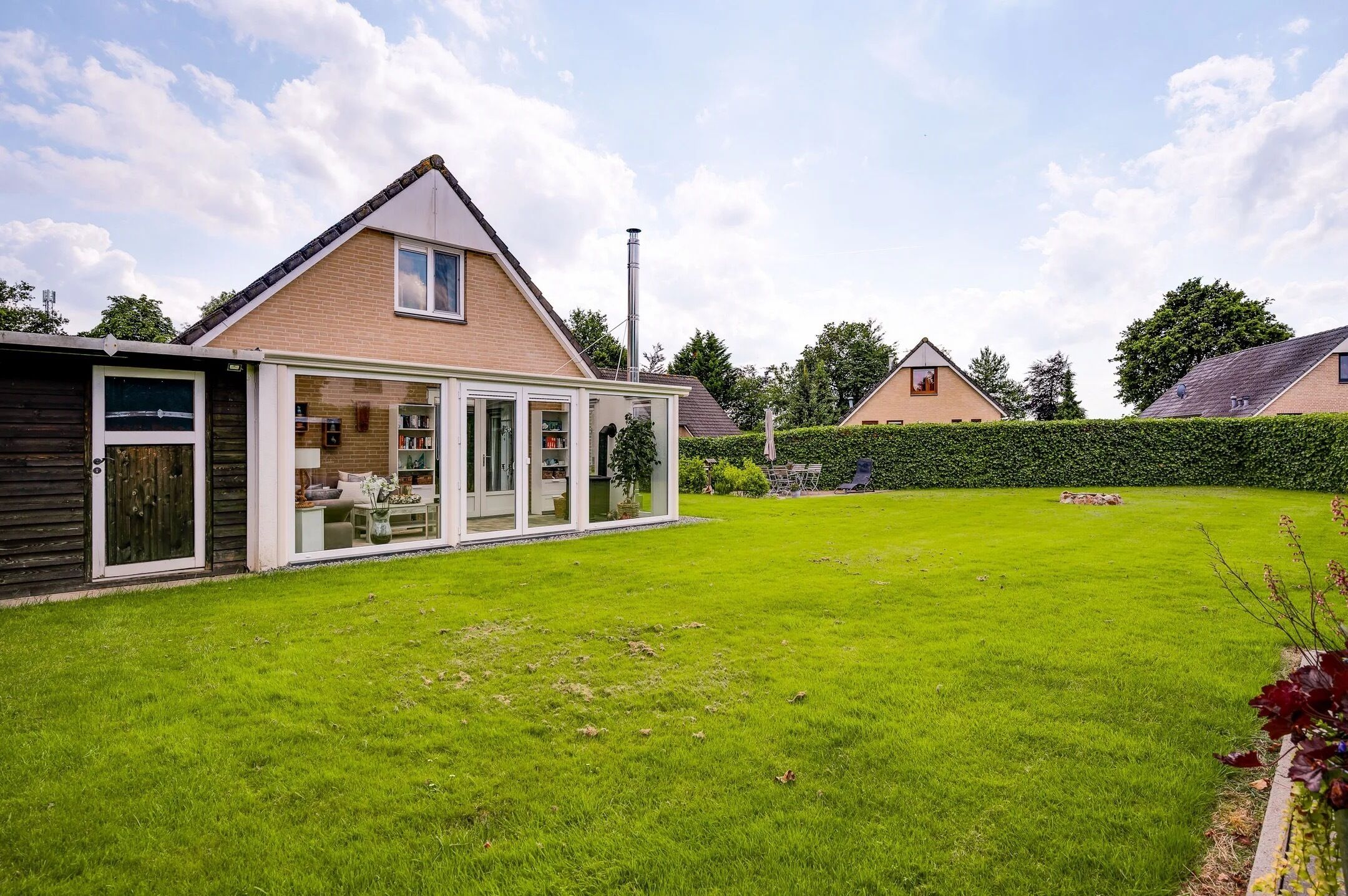 A residential property with a large glass conservatory, a well-maintained lawn, and a brick house in the background.