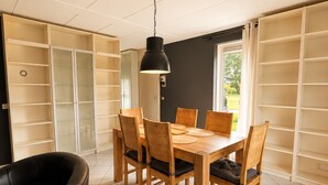 A dining area with a wooden table and chairs, a black leather sofa, and built-in shelving. - Vacation villa with conservatory at the 't Posterbos park (Posterholt)