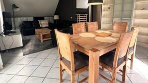 A dining area with a wooden table and chairs, a hanging light fixture, and a black sofa in the background. - Vacation villa with conservatory at the 't Posterbos park (Posterholt)