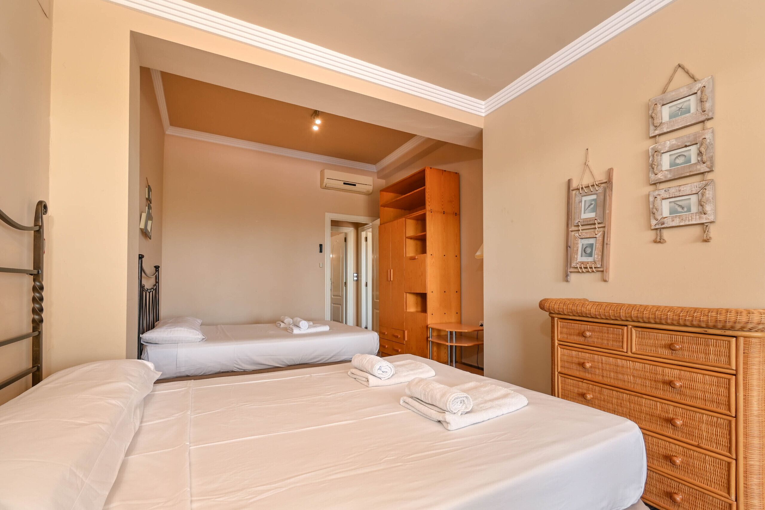 A hotel room with a bed, a wooden wardrobe, a small table, and a wall-mounted picture frame.