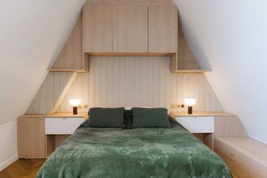 A bedroom with a sloped ceiling, a bed with a green blanket, two bedside tables with lamps, and a wooden headboard. - High-end 2 bedroom duplex with parking Place Morny (Deauville)