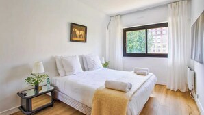 Ein Hotelzimmer mit einem Bett, einem Nachttisch mit Lampe, einem Fenster mit Vorhängen und einem gerahmten Bild an der Wand.