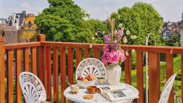 Eine Holzterrasse mit gedecktem Tisch, umgeben von Grünflächen und Gebäuden im Hintergrund.