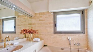 Ein modernes Badezimmer mit einem Doppelwaschbecken, einer Badewanne, einem großen Spiegel und einem Fenster.