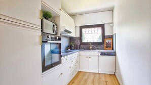 Eine kompakte Küche mit weißen Schränken, einem Backofen, einer Mikrowelle und einem Fenster mit Blick auf Gebäude.