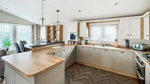 A modern kitchen with a central island, built-in cabinets, a herringbone wood floor, and pendant lighting. - Willerby Portland - UKC9613 (Towyn)