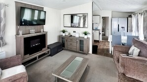 Een moderne woonkamer met een flatscreen televisie, een salontafel, banken, een keukenhoek en een eethoek.