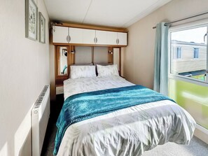 A bedroom with a bed, a wardrobe, a radiator, and a window with a view of a building. - ABI St David - UKC9615 (Towyn)