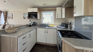 Cocina compacta con microondas, estufa, lavaplatos y armarios de madera.