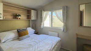 Un dormitorio con cama, mesita de noche, radiador, ventana con cortinas y espejo.