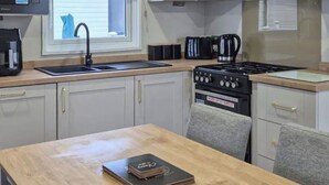 A kitchen with a sink, stove, cabinets, and a dining table with a book. - Sunseeker Y Wyddfa - UKC9637 (Towyn)