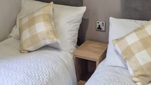 A double bed with white bedding and beige checkered pillows, a wooden nightstand, and a wall socket. - Sunseeker Y Wyddfa - UKC9637 (Towyn)