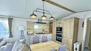 Cocina compacta con estufa a gas, horno y microondas, una mesa de comedor con sillas y un refrigerador pequeño.