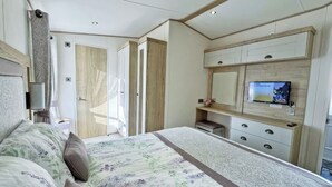 Un dormitorio con cama, televisor, tocador con cajones y espejo.