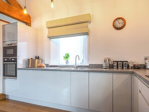 Eine moderne Küche mit Einbauofen, einem Edelstahl-Kühlschrank, einem Fenster mit Pflanze und einer Uhr an der Wand.