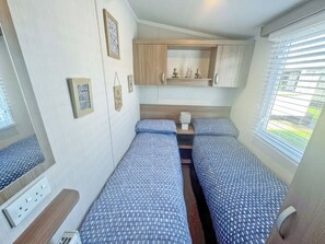 Interior compacto de una caravana con dos camas, una pequeña cocina y una ventana con persianas.