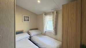 Una camera da letto piccola e ordinata con due letti singoli, una finestra con tende, un quadro appeso al muro e un armadio in legno.