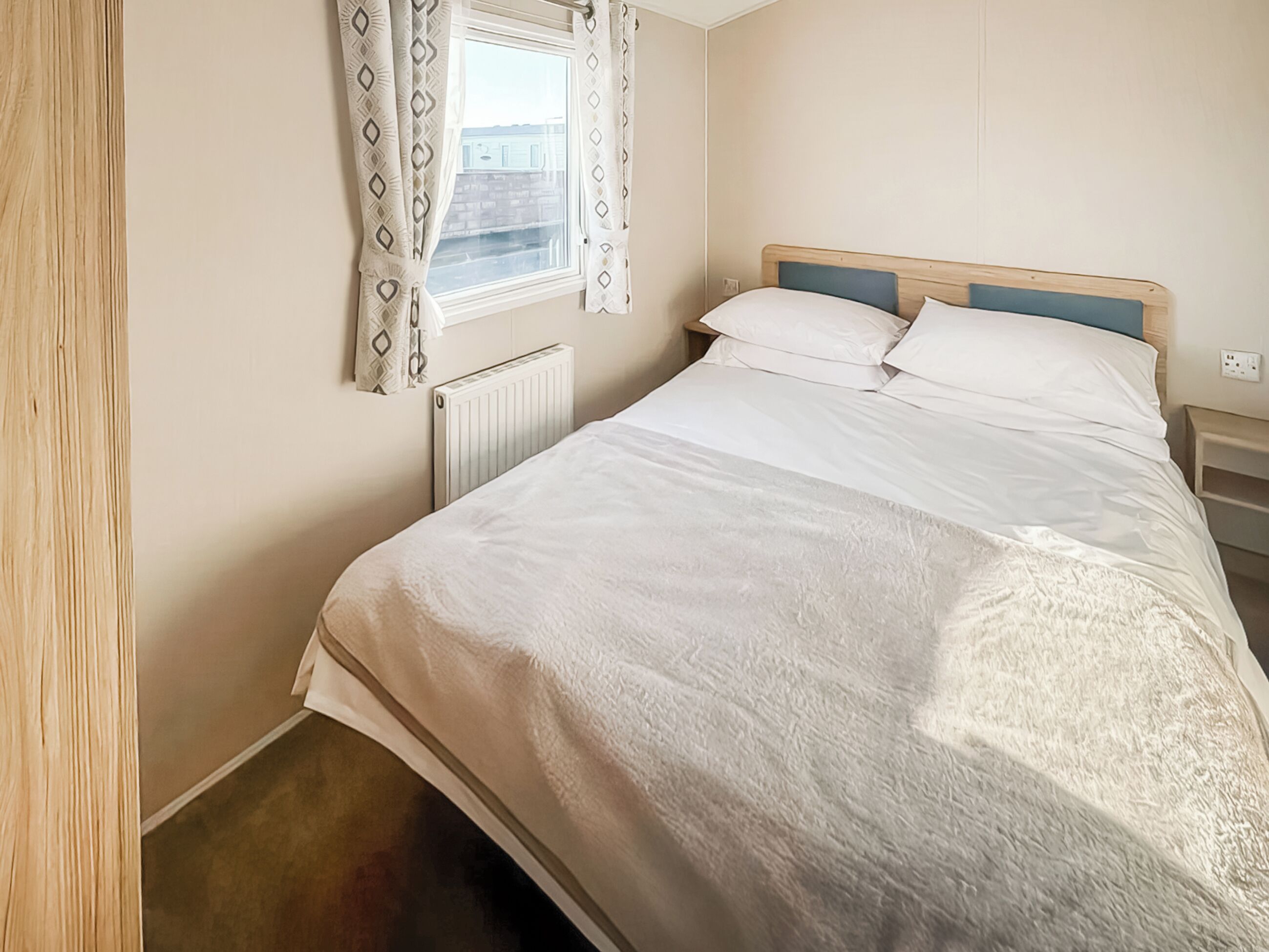 A bedroom with a bed, a window with curtains, a radiator, and a nightstand.