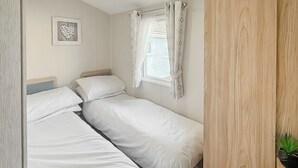 Quarto com duas camas individuais, uma janela com cortinas, um quadro na parede e um guarda-roupa de madeira.