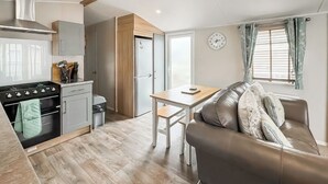 Cozinha compacta com fogão, forno e armários, sala de jantar com mesa e cadeiras, e sala de estar com sofá e janela.