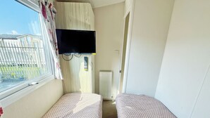 Une chambre avec deux lits, un téléviseur fixé au mur, une fenêtre avec des rideaux et un radiateur.