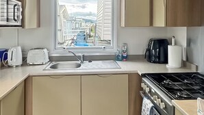 A kitchen with a window view, a sink, a toaster, a kettle, and a stove. - Swift Escape - UKC9641 (Towyn)