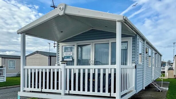 A mobile home with a covered porch and a sign indicating it is a caravan for hire. - Swift Escape - UKC9641 (Towyn)