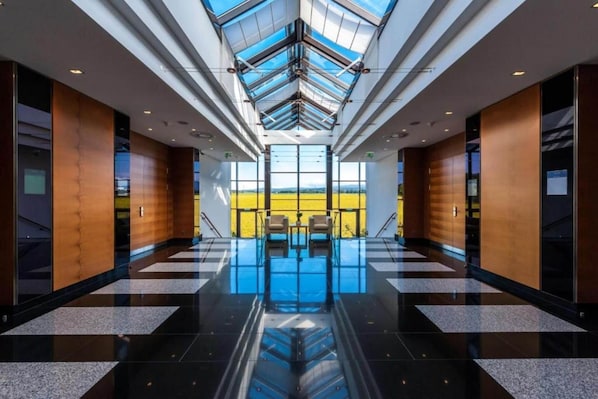 A modern hotel lobby with a glass ceiling, a checkered floor, and a view of the outdoors.