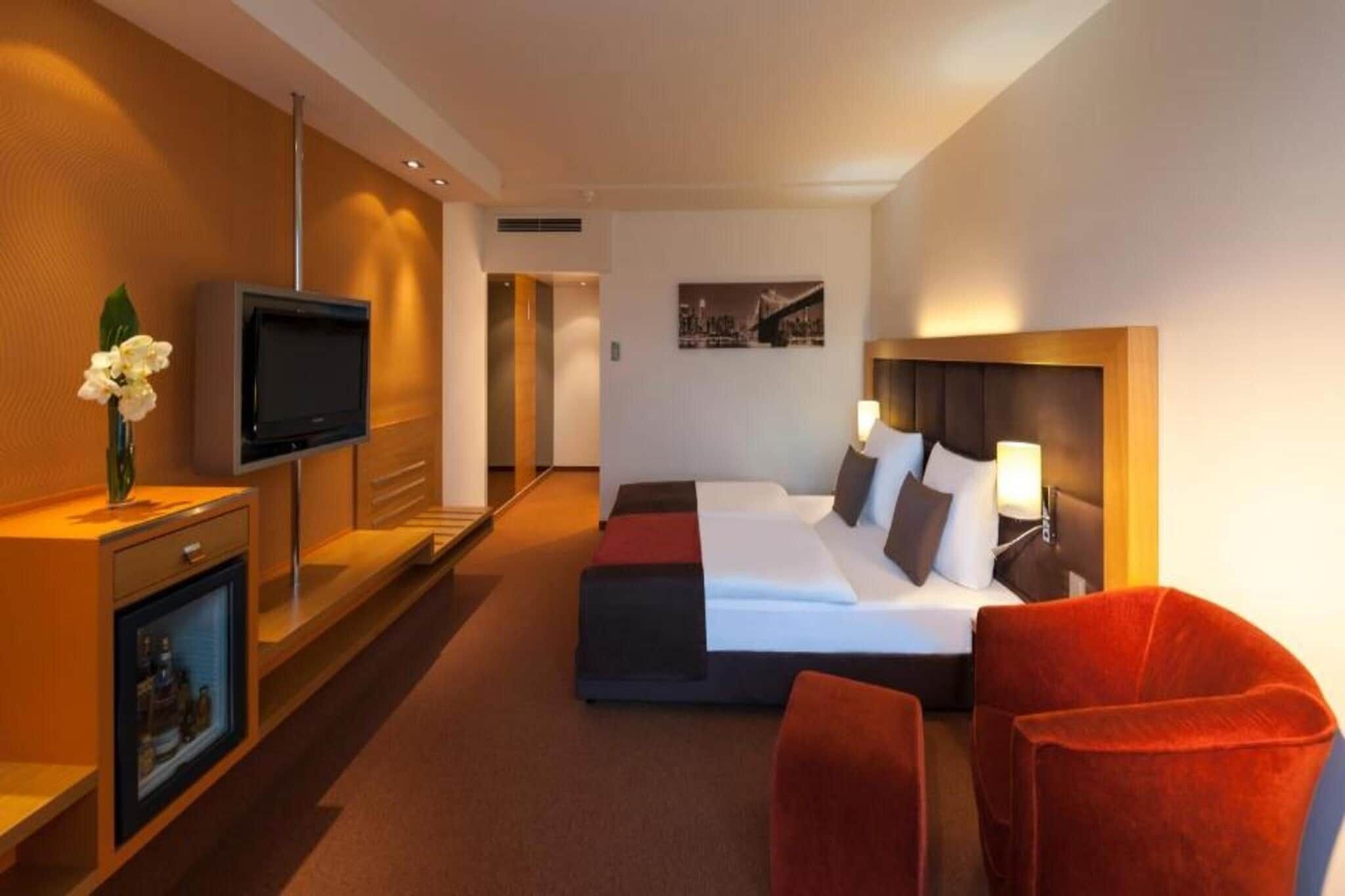 Una habitación de hotel con cama, televisor, escritorio y computadora, y una silla roja.