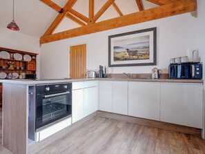 A kitchen with wooden beams, white cabinets, a built-in oven, a sink, and a coffee maker.