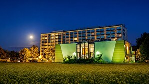 Un hotel de varios pisos con un diseño moderno, que destaca por una fachada de vidrio y una pared verde de acento.