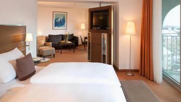 Habitación de hotel con cama, sofá, televisión y escritorio con lámpara.