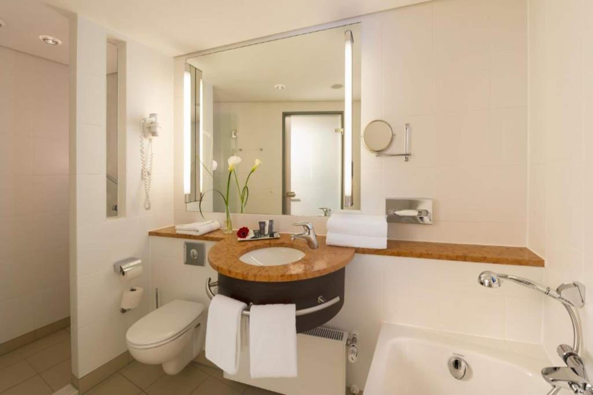 Un baño moderno con un lavabo redondo, un inodoro, una bañera y un espejo grande.
