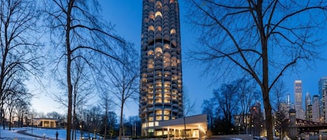 A tall building with a unique architectural design, surrounded by a park with pathways and benches.