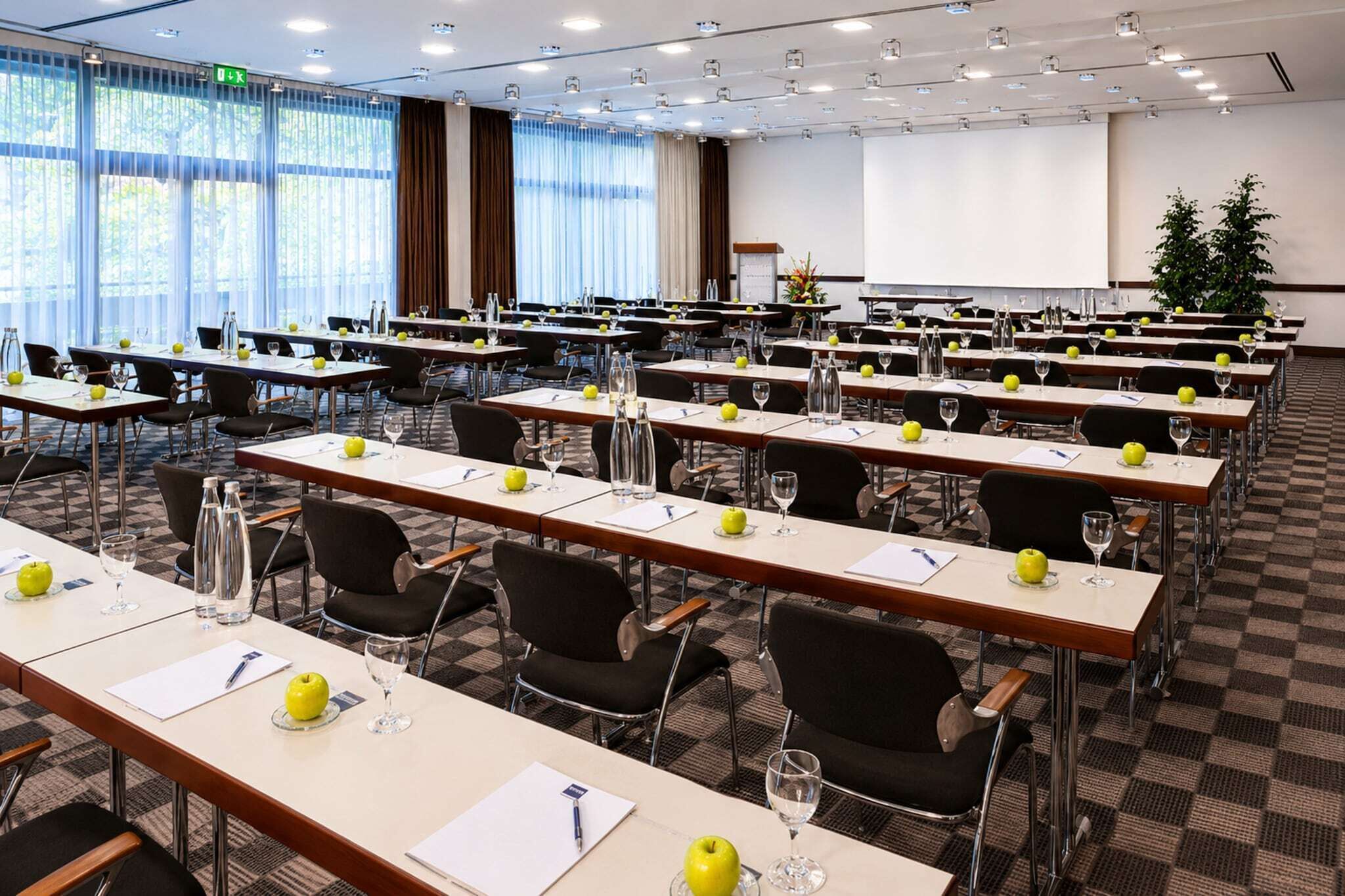 A conference room with multiple tables, chairs, and a projector screen.