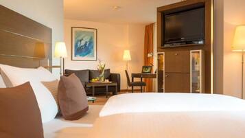 A hotel room with a large bed, a desk with a laptop, a television, and a painting on the wall.