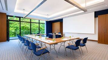 A conference room with a large table, chairs, a projector screen, and a view of greenery outside.