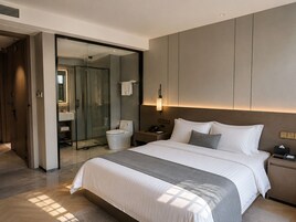 Habitación de hotel moderna con una cama grande, una mesita de noche, una ducha de vidrio y un baño visible.