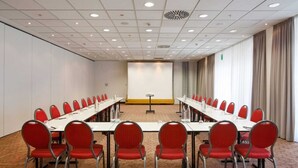 Une salle de conférence avec une longue table, des chaises rouges et un écran de projection.