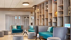 Un hall d’entrée moderne avec un canapé, des fauteuils, des poufs et une bibliothèque.