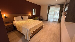 A modern hotel room with a large bed, bedside tables, a desk, and a large window with curtains.