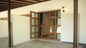 A covered outdoor area with a concrete floor, wooden-framed sliding doors, and a wall-mounted light fixture.