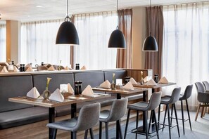 Un espace de salle à manger moderne, doté d’une longue table, de nombreuses chaises et de luminaires suspendus.