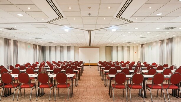 A conference room with rows of tables and chairs, a podium, and a large screen.