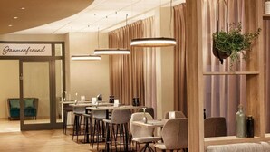 A modern dining area with a long table, multiple chairs, pendant lights, and a plant on a shelf.